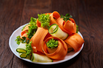 Artistically served vegetable salad with carrot, cucumber, letucce over wooden background, selective focus