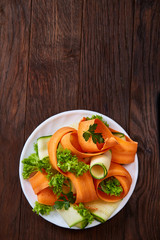 Artistically served vegetable salad with carrot, cucumber, letucce over wooden background, selective focus