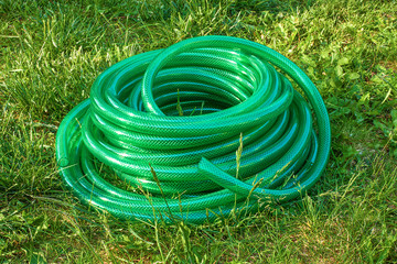 Watering garden hose bundle on the lawn in the garden. Long pvc green garden hose on grass in...