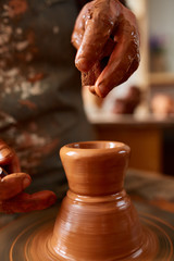 Adult male potter master modeling the clay plate on potter's wheel. Top view, closeup, hands only.
