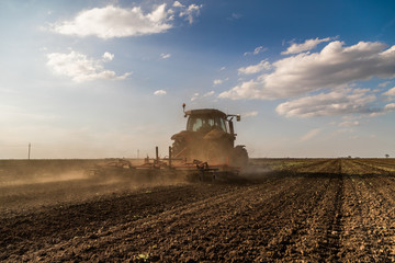 Fototapeta premium Tractor cultivating field at spring