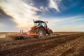 Foto op Plexiglas Tractor Trekker cultiveren veld in de lente