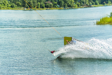wakeboarder jumps from a springboard behind a rope and makes a wave on the water
