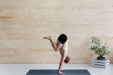 Sporty man practices yoga handstand asana Adho Mukha Vrikshasana at the yoga studio. Balance...