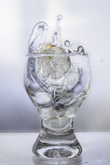 Splash water in a glass with a lemon on a gray background