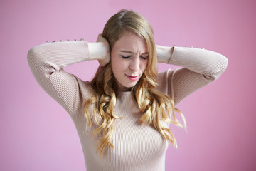 Stress and depression concept. Picture of frustrated beautiful young Caucasian female with long blond wavy hair covering her ears, can't stand loud sounds because of terrible headache or migraine