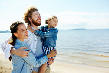 Happy family of three embracing while enjoying hot summer day on the beach at leisure