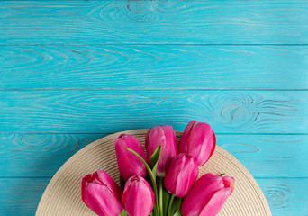 Women's accessories - hat and bouquet of pink tulips on a wooden background.