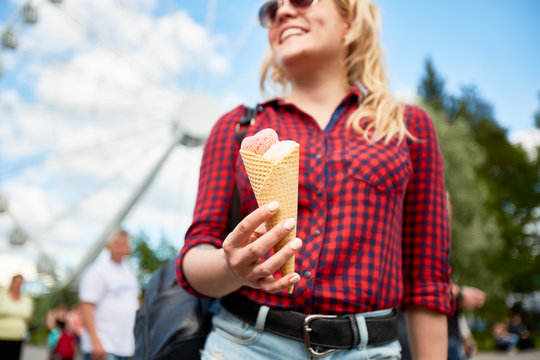 Yummy double-topping ice cream in hand of casual blond girl visiting modern amusement park on summer day
