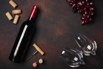 Bottle of wine, two glasses, corkscrew and corks, on rusty background top view