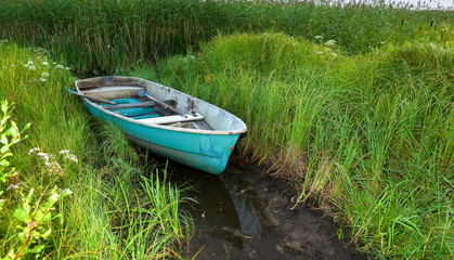 Old green plastic fishing boat at the lake in green grass