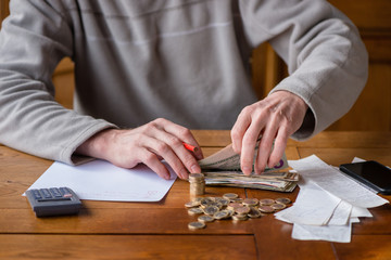 Close up man with calculator counting, making notes at home, hand is writes in a notebook. Stacked coins arranged at deesk. Savings finances concept.
