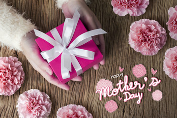 Mother's day concept of young woman hands holding pink gift box and carnation flower on wooden table