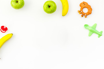 Healthy nutrition for babies. Apple, banana near toys on white background top view copy space