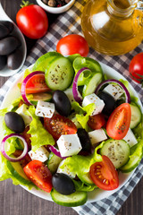 Fresh Greek salad made of cherry tomato, ruccola, arugula, feta, olives, cucumbers, onion and spices. Caesar salad in a white bowl on wooden background. Healthy organic diet food concept.