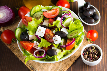 Fresh Greek salad made of cherry tomato, ruccola, arugula, feta, olives, cucumbers, onion and spices. Caesar salad in a white bowl on wooden background. Healthy organic diet food concept.