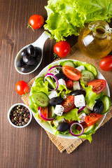 Fresh Greek salad made of cherry tomato, ruccola, arugula, feta, olives, cucumbers, onion and spices. Caesar salad in a white bowl on wooden background. Healthy organic diet food concept.