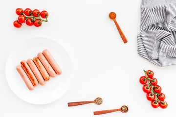 Grilled sausages on white table near cherry tomatoes and spices in wooden spoons top view copy space