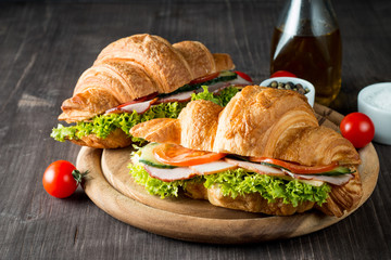 Fresh croissant or sandwich with salad, ham, jamon, prosciutto, salami, cheese, chicken, tomatoes on wooden background. Morning breakfast concept. Healthy and fast food.