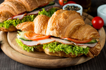 Fresh croissant or sandwich with salad, ham, jamon, prosciutto, salami, cheese, chicken, tomatoes on wooden background. Morning breakfast concept. Healthy and fast food.