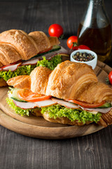Fresh croissant or sandwich with salad, ham, jamon, prosciutto, salami, cheese, chicken, tomatoes on wooden background. Morning breakfast concept. Healthy and fast food.