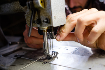 Middle-aged man working in his workshop with his hands sewing clothes shining in the evening sun close-up