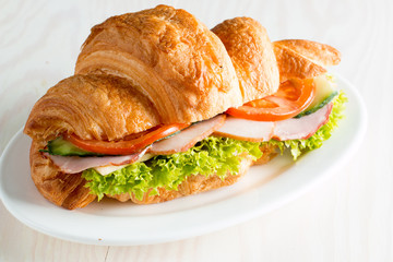 Fresh croissant or sandwich with salad, ham, jamon, prosciutto, salami, cheese, chicken, tomatoes on wooden background. Morning breakfast concept. Healthy and fast food.