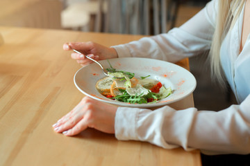 hands of the girl who has a salad from a white round dish