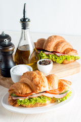 Fresh croissant or sandwich with salad, ham, jamon, prosciutto, salami, cheese, chicken, tomatoes on wooden background. Morning breakfast concept. Healthy and fast food.