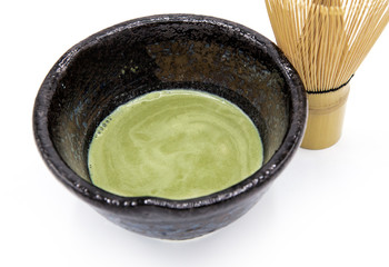 Organic matcha green tea in a Japanese ceramic tea cup with a bamboo tea whisk on white background