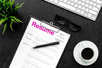 Review resumes of applicants. Resume on black work desk with coffee, glasses, keyboard top view