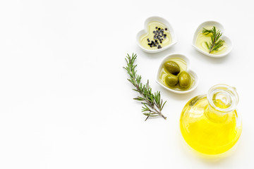 Fresh olive oil in glass jar near green olives and branch of rosemary on white background top view copy space