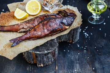 Smoked fish with lemon slices on backing paper on dark wooden smoking background, top view, copy...
