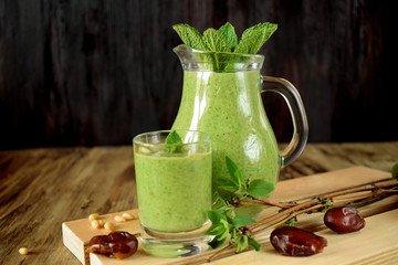 Green smoothie in a glass and in a jug on wooden background