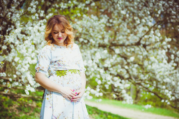 Fototapeta na wymiar Beautiful pregnant woman walking in the flowers garden in the spring