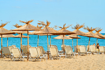 A large clean sea beach with sun loungers and thatched umbrellas for tourists on a bright sunny summer day against a blue sea and blue sky                               