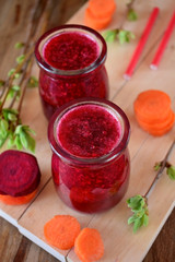 Red vegetable smoothie made of carrot and beetroot in glass jars on wooden background