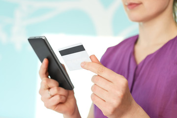 Online shopping concept. Close up of unrecognizable female model holds modern mobile phone and credit card, surfes internet webstore, pays for purchase in internet, isolated over blue background