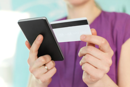 Selective focus on woman`s hands hold modern black cell phone and plastic card, makes shopping online or checks her bank account in internet, connected to wifi. People and online transactions