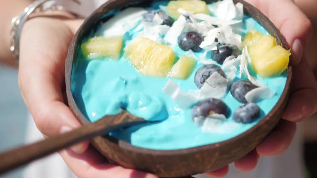 hands holding blue majik smoothie bowl approaching camera lens