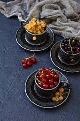 Composition of fresh ripe berries: red, black and white currants on a dark gray concrete background. Dark photo. Photographing in natural light. Space for your text.