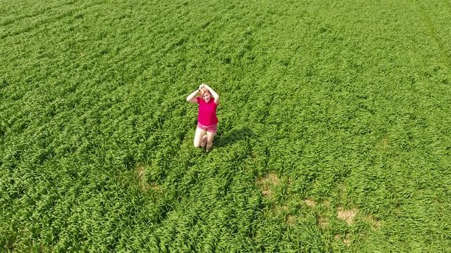 A woman in a red T-shirt poses in front of the drony camera. He runs away from the camera and runs after her. Fun and sports on a wheat field