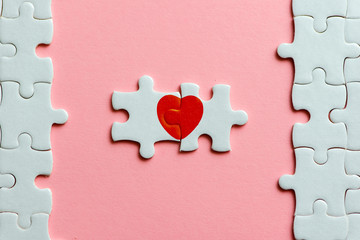 two pieces of a puzzle with red heart on pink background