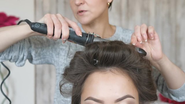 Makeup artist stylist works with model. hairdresser does the hair styling of the model. woman is working a styler with the girl's long hair. The hairdresser makes curls on the girl's straight hair.