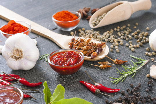 fresh and dried chili fruits, peppercorn, pepper powder, sauce and garlic, bay leaves on old black wooden table background