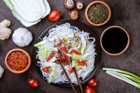 Rice noodles with vegetables, mushrooms and soy sauce in the ceramic plate  on dark background. Flat lay