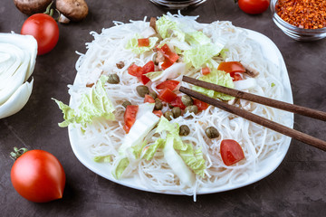 Rice noodles with vegetables, capers and soy sauce in the ceramic plate  on dark background.
