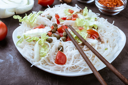Rice noodles with vegetables, mushrooms and soy sauce in the ceramic plate  on dark background.
