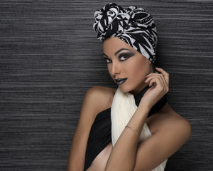 beauty girl with turban and black and white makeup in front of a black strings background with earrings