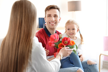 Happy woman receiving flowers from husband and daughter at home. Mother's day celebration